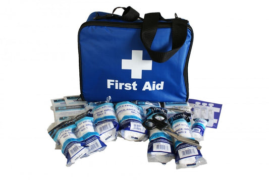 A blue first aid grab bag with various first aid items like dressings, cleansing wipes, and safety pins laid out in front.